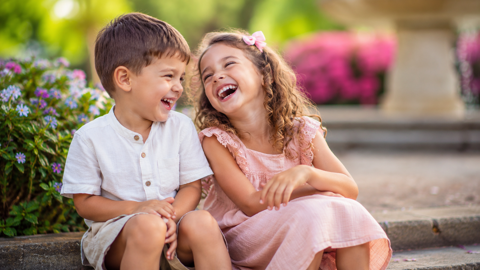 Two children laughing together in a cheerful garden setting